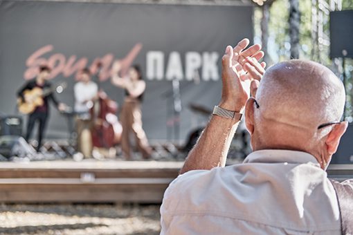 Mature man applauds, raising his hands high. Concert on summer stage in city park. entertainment