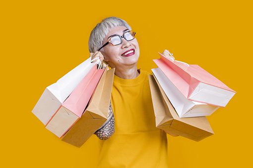 Asian happy senior female woman tattoo holds colourful shopping packages standing on yellow background studio shot, Close up Portrait old female hand hold shopping bags enjoy shopping with joyful outlet malls and shopping