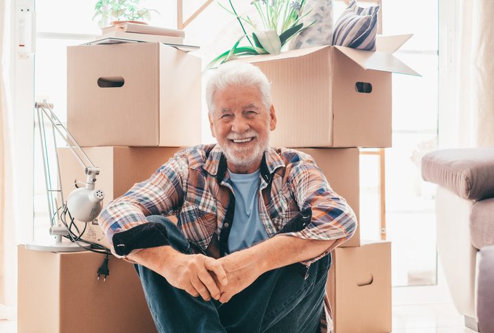 Older man smiling in front of moving boxes in home